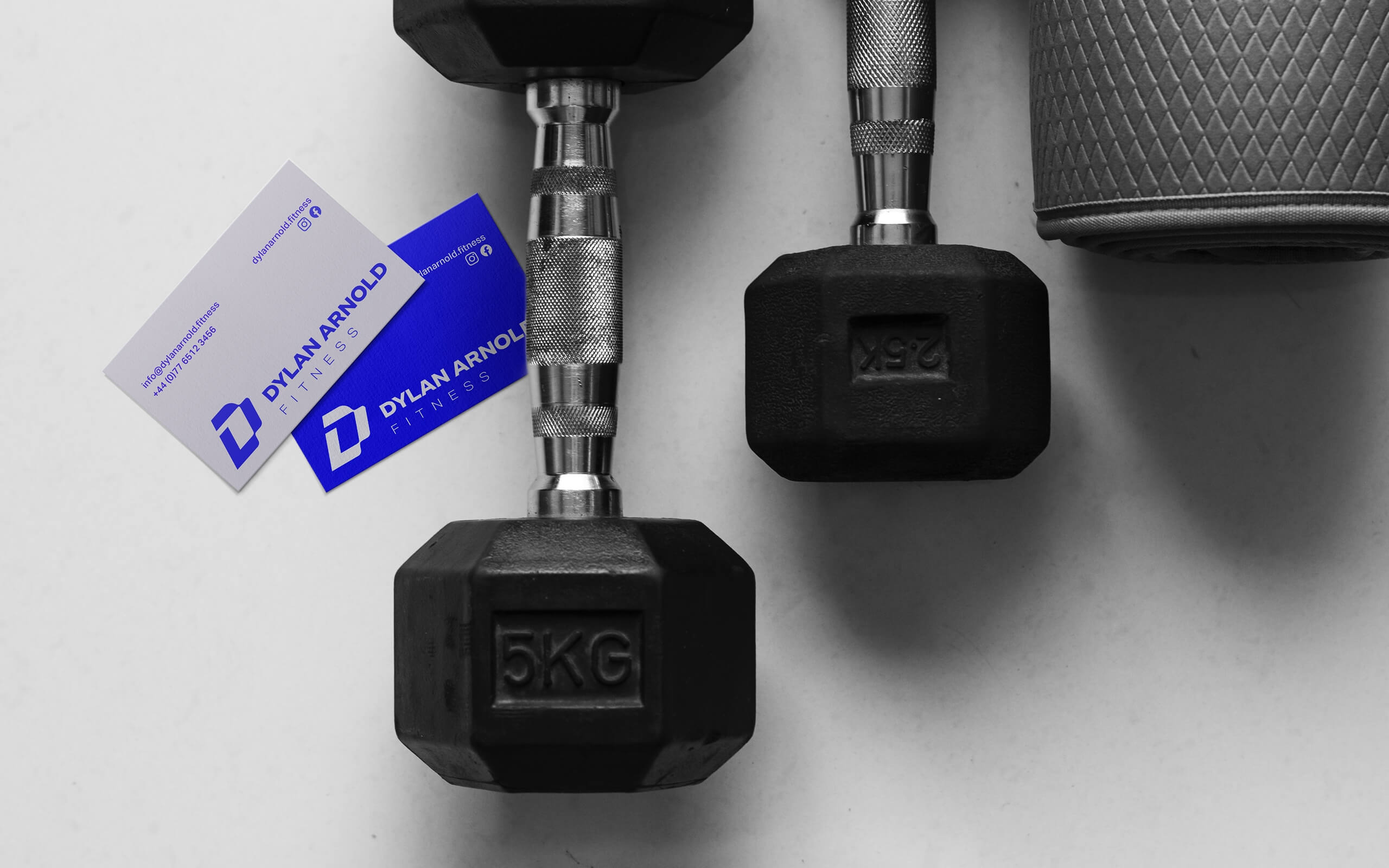 Top down view of two 5kg dumbbells, a grey yoga mat and two Dylan Arnold Fitness business cards