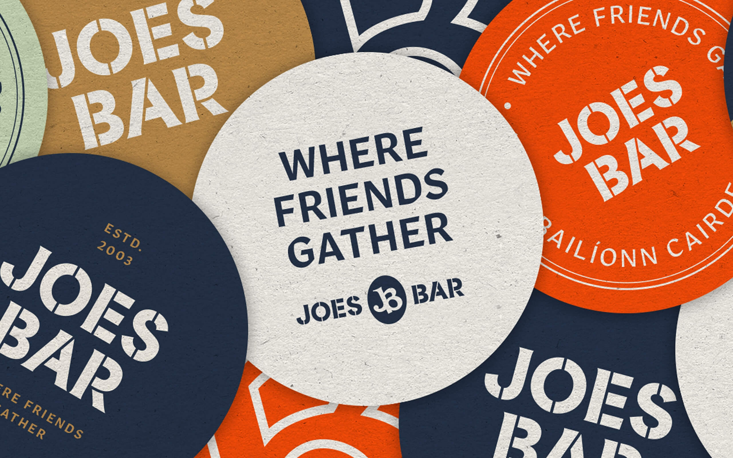 Top down view of beer mats belonging to Joe's Bar. Off-White, navy, orange and light green in colour feating logos and the slogan 'where friends gather'. 